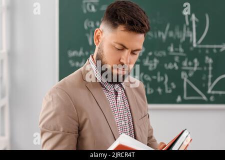 Handsome Math teacher reading book in classroom Stock Photo