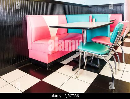 An interior of a classic American 1950s style diner with colorful stools and checkered floor Stock Photo
