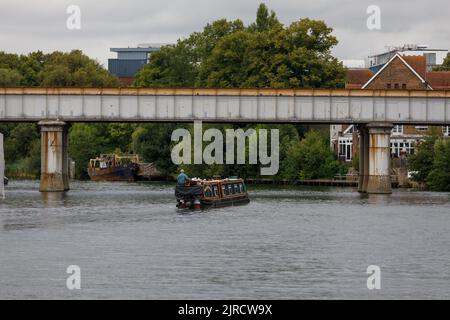 A traditional English barge boat travels along the River Thames, under the iron railway bridge in Staines upon Thames on summer's day Stock Photo