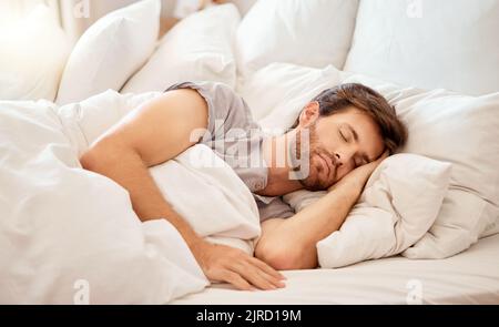 Relax, sleep and peace of a tired man sleeping in a bedroom bed at home. Dreaming, relaxing and resting calm attractive person with closed eyes on a Stock Photo