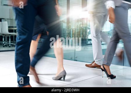 Just another busy day in the office. a group of unrecognizable businesspeople walking through the office. Stock Photo