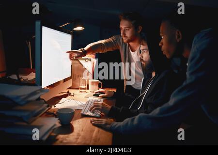 Three programmers are better than one. young computer programmers working late in the office. Stock Photo