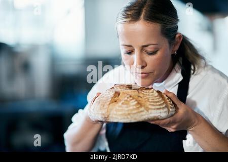 Baker, pastry chef and cafe owner smelling a loaf of fresh baked bread in the kitchen of her coffee shop. Closeup of a female cook enjoying the aroma Stock Photo