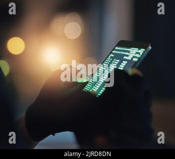 Theres no system he cant crack through. an unrecognisable hacker using a cellphone in the dark. Stock Photo