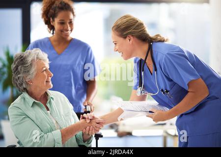 Making sure she gets the best help she deserves. a doctor holding medical records and shaking hands with a smiling senior woman sitting in a Stock Photo