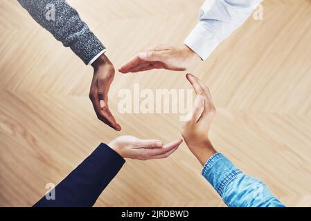 What goes around comes around. High angle shot of a group of unidentifiable businesspeople forming a circle with their hands. Stock Photo