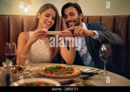 Delicious food to match the mood. a happy young couple taking a picture of their meal on a cellphone during a romantic dinner date at a restaurant. Stock Photo