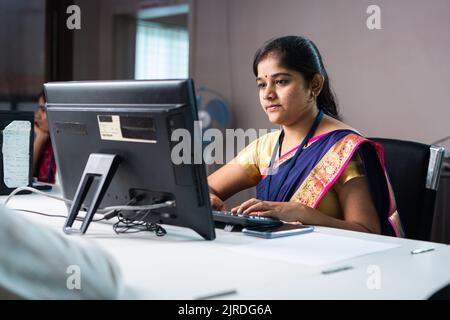 Serious bank employee busy working on computer in front of customer - concept of woman empowerment, job or career and banking service. Stock Photo