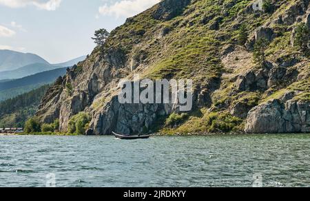 Man on fishing wooden longboat with motor moving to tent camp along cliff. Lake Baikal, Russia. Stock Photo