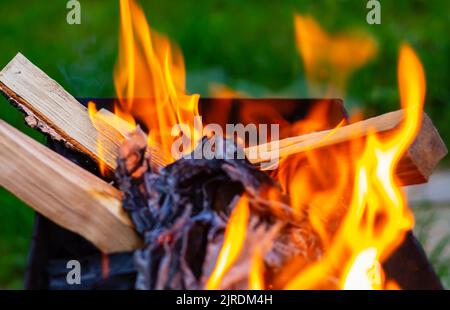 Tongues of orange fire from burning wood sticks. Preparation of embers for preparing of appetizing, delicious barbecue on grill in nature on blurred g Stock Photo