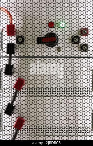 Industrial lithium-ion batteries for uninterruptible power supplies in battery cabinet. View through steel honeycomb mesh safety door. Selective focus Stock Photo