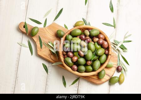 Mixed olives in wooden bowl on white planks background Stock Photo