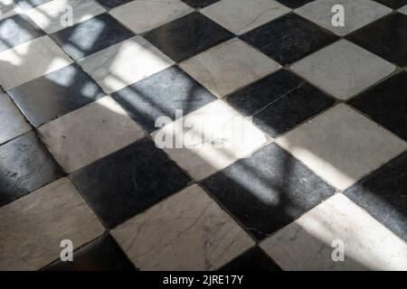 Light and shadow on an antique black and white checked stone tiled floor. Stock Photo
