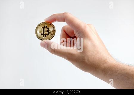 A man's hand holds a gold bitcoin, isolated on a white background. Stock Photo