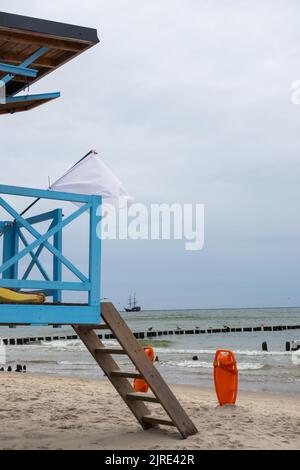 A blue lifeguard booth on the beach on a cloudy day. orange lifeboats stuck in the sand next to it Stock Photo