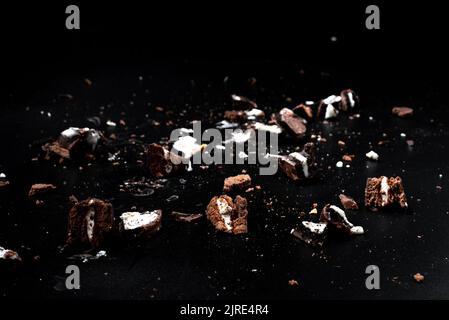Scattered crumbs of chocolate sandwich cookies filled with sweet cream flavored isolated on black background. Stock Photo