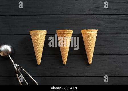 Three waffle cups for ice cream empty on a black wooden background view from above. Next to the ice cream scoop Stock Photo