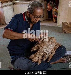 Man sits cross-legged on floor while finishing carving wooden mask. Stock Photo