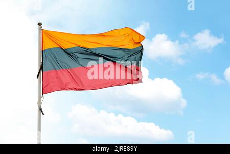 Large Lithuanian national flag on flagpole waving in wind against blue cloudy sky Stock Photo