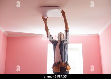 Handsome young builder is twisting the light bulb in. The man is looking up. Stock Photo