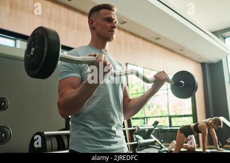 Young man lifting barbell during his sport training in gym Stock Photo