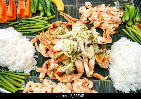 Boodle fight is a Filipino social meal or buffet eaten using hands seen here including crab, prawns, okra, asparagus and boiled rice. Stock Photo