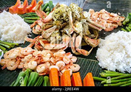 Boodle fight is a Filipino social meal or buffet eaten using hands seen here including crab, prawns, okra, asparagus and boiled rice. Stock Photo