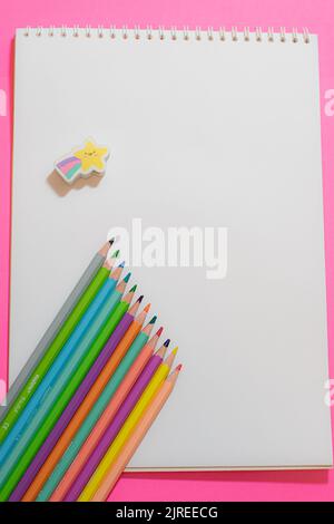 Top view of colored pencils and drawing pads on pink background. Blank space to wirte Stock Photo