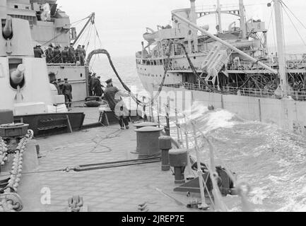 HMS JAMAICA refuelling at sea from a tanker, September 1944. Looking aft as HMS JAMAICA and a tanker proceed with refueling still in progress. In the foreground is a rating holding a marked line which enables the navigator watching from the bridge to keep a true course during the operation. Part of the cruiser's rear six inch gun turrets can be seen. Stock Photo