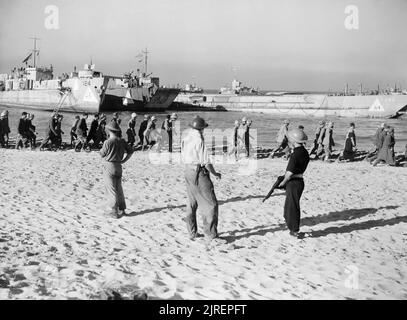 Italian POWs march to waiting landing craft during the Allied invasion of Sicily, July 1943. Prisoners of war marching along the beach to awaiting ships, watched by Naval Commandos, one of whom is armed with a Tommy gun at dawn of the opening day of the invasion of Sicily. A landing craft infantry (large) (LCI (L) 124) and two landing craft tanks LCT 382. Stock Photo