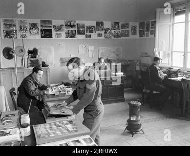 Royal Air Force- Italy, the Balkans and South-east Europe, 1942-1945. Interior of the Photographic Office of the RAF Public Relations (Oversea) Unit at Allied Forces Headquarters at Caserta, Italy, where personnel are seen sorting and captioning prints of RAF official photographs for distribution to the news media. Left to right are: Sergeant A Collins of Manchester; Corporal M E N Holmes of Southall, Middlesex; Flight Lieutenant L H Baker of Stanmore Middlesex, an Air Ministry official photographer in charge of the section, and Leading Aircraftman P J McSherry of London. Stock Photo
