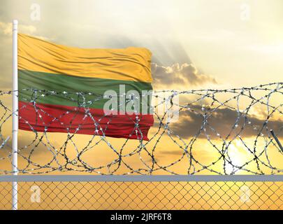 Flagpole with the flag of Lithuania against the sky and behind a fence with barbed wire. The concept of protecting the borders of territories. Stock Photo