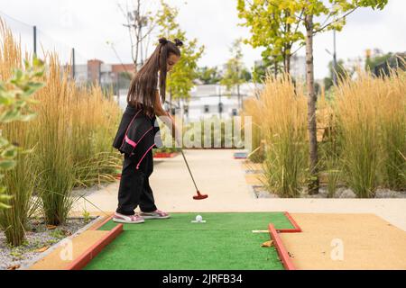 Miniature golf outdoor. Little caucasian girl golfing in the mini golf course. Stock Photo