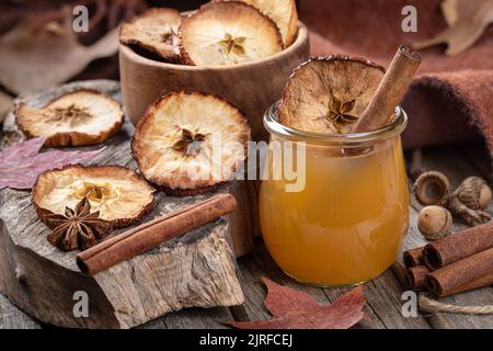 Glass of apple cider with cinnamon stick and dried apple chip on an old rustic table Stock Photo