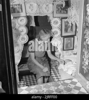 British Canals in Wartime- Transport in Britain, 1944 A mother settles her baby down to sleep in the cabin of her canal boat. The cabin is adorned with decorative plates, family photographs and lace, which, according to the original caption 'are the hallmarks of a good canal boat cabin'. Stock Photo