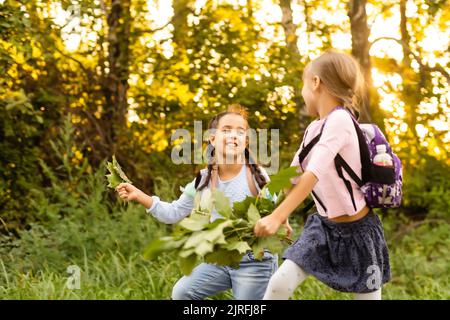Schoolgirls picking autumn leaves for drying. School project making herbarium from dried leaves. Girl prepared leaves for autumn craft. girls walking Stock Photo