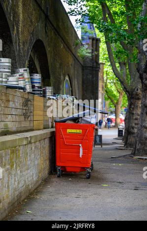 LONDON - May 20, 2022: Large red wheeled bin over loaded at side of street near Waterloo Station Stock Photo