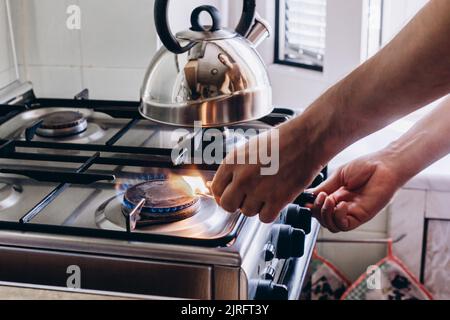 A man's hand with a match lights a gas burner or a gas stove in the kitchen. Stock Photo