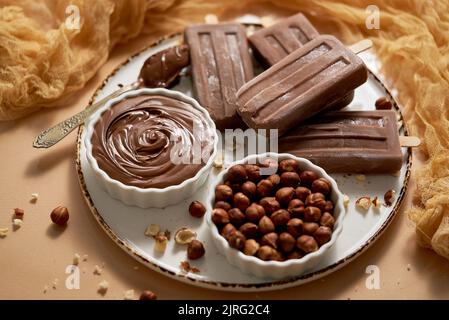 Chocolate popsicles with hazelnuts served with melted chocolate on a white plate Stock Photo