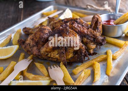 Crispy Spatchcock chicken with french fries on a baking tray Stock Photo