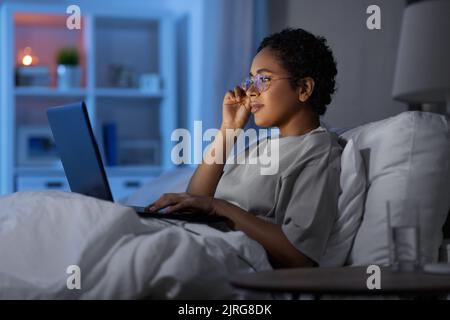 woman with laptop in bed at home at night Stock Photo