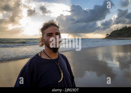 Middle-aged bearded man on the beach during sunrise with defiant look. Stock Photo