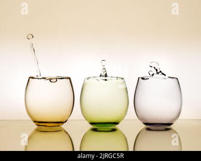 Water falls. Drips in three colourful glasses. Stock Photo