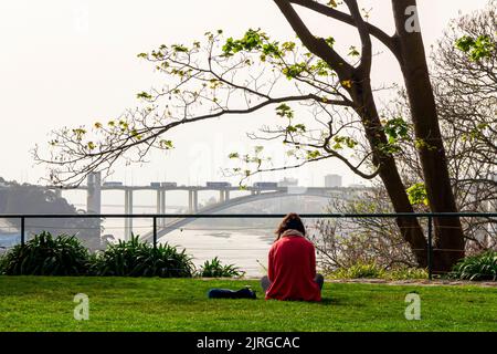 Young woman relaxing in the Jardim do Palacio de Cristal gardens in Porto in northern Portugal with the River Douro and bridge in the distance. Stock Photo