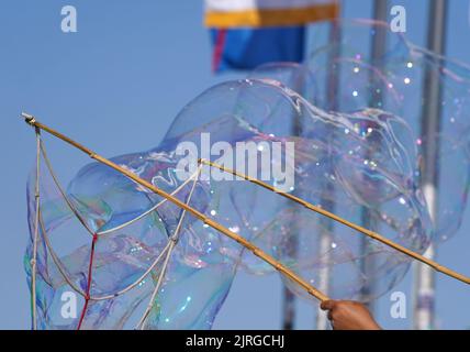Hamburg, Germany. 24th Aug, 2022. A woman pulls giant soap bubbles into the air at Jungfernstieg in the city center. Credit: Marcus Brandt/dpa/Alamy Live News Stock Photo