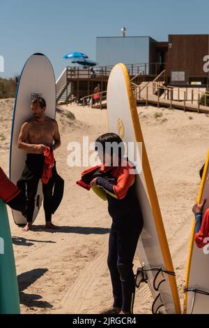 Aveiro, Portugal - August 19, 2022: people with wetsuits and pick up surfboards at the secreto surf school facilities. Stock Photo