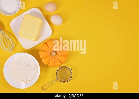 Pumpkin pie ingredients and baking tools on yellow background with copy space Stock Photo