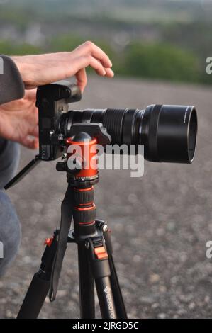 A vertical shot of hands operating an Olympus MFT camera standing on a tripod with telephoto lens Stock Photo