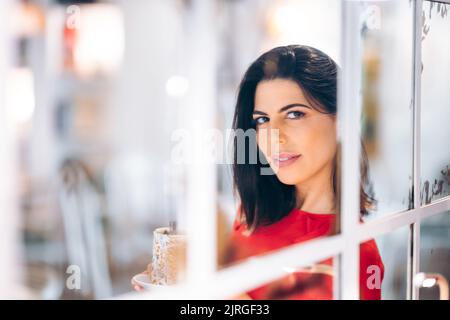 Attractive woman looks seductively through a window with a coffee seen from outside Stock Photo