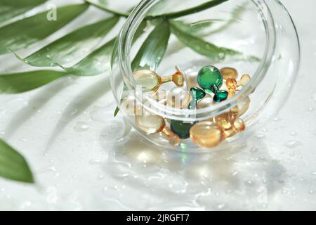 Serum capsules for healthy skin. Blurred background, glass jar with the capsules and green palm leaf Stock Photo